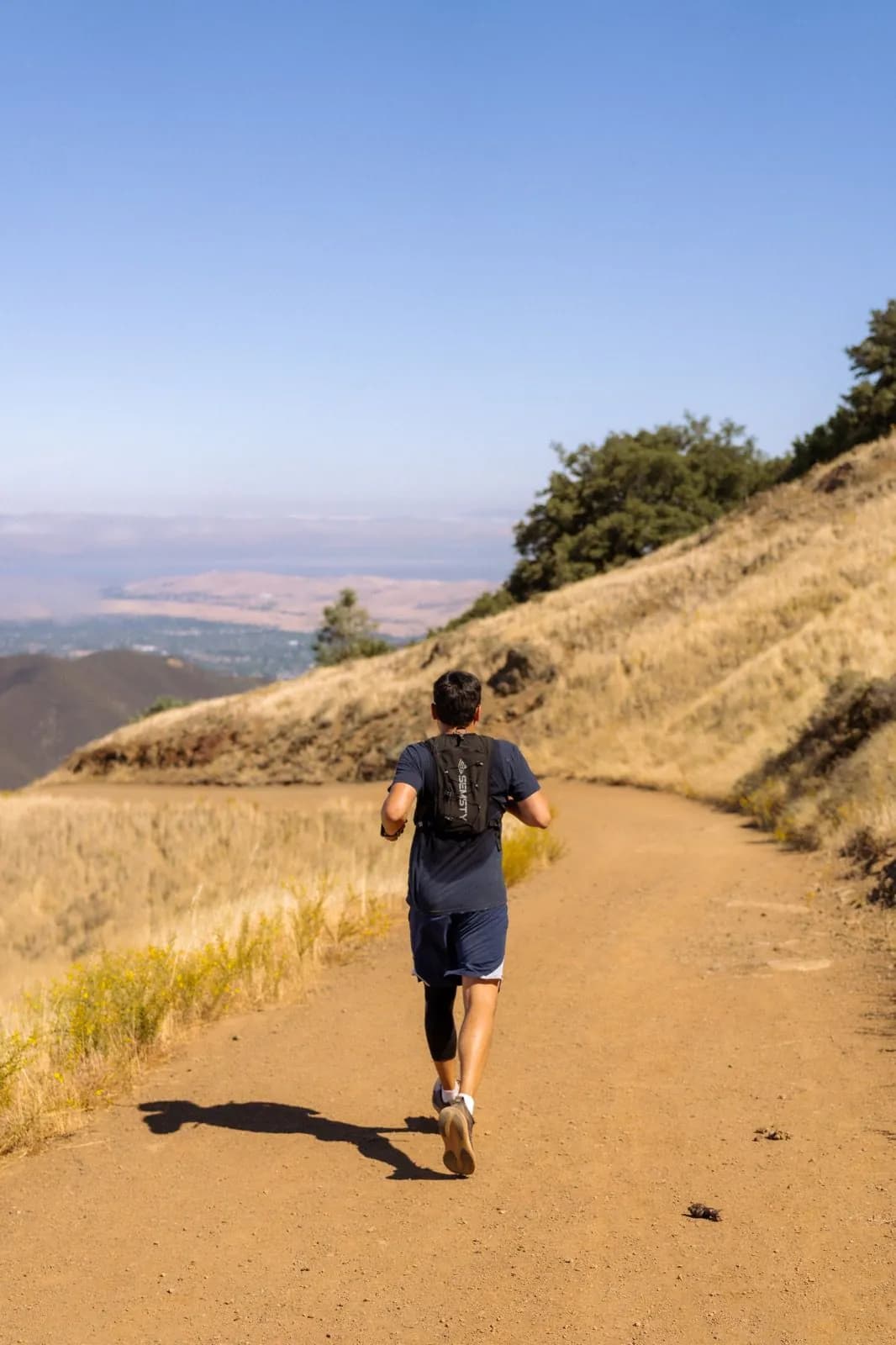Runner descending a wide trail with scenic East Bay views
