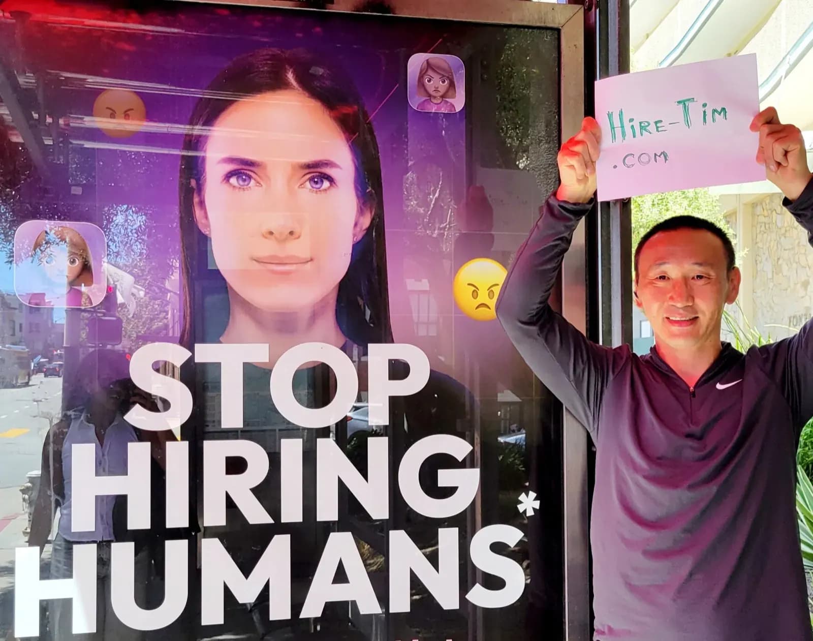 Tim Baz holding a HireTim.com sign next to a Stop Hiring Humans poster in San Francisco